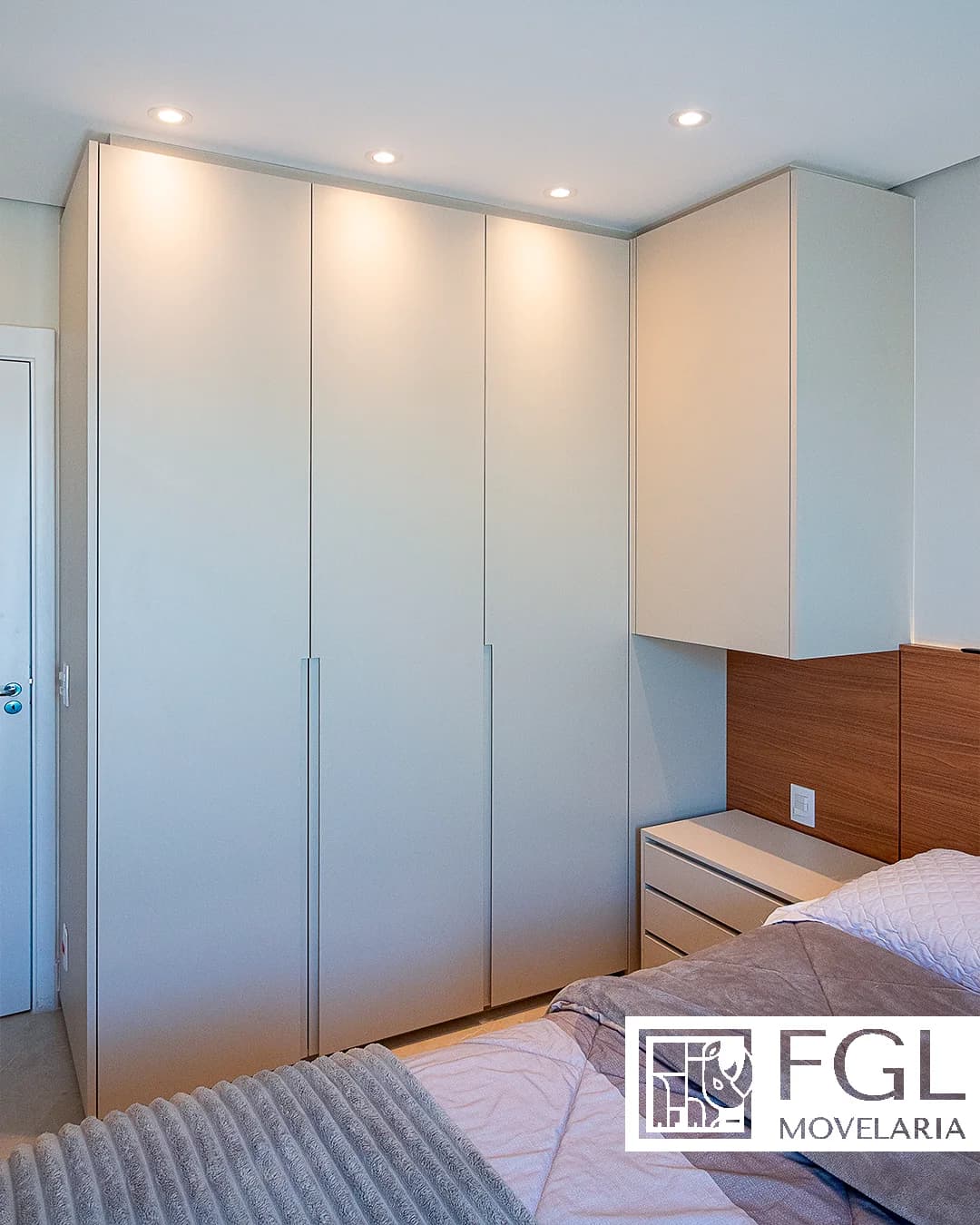 Dormitório com guarda-roupa claro, armário aéreo e cabeceira amadeirada